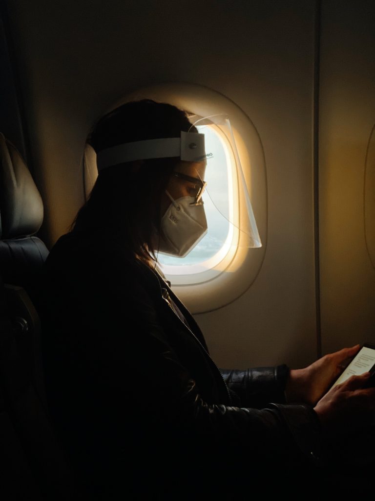 Mujer usando careta y cubrebocas para disminuir el riesgo de contagio en un avión