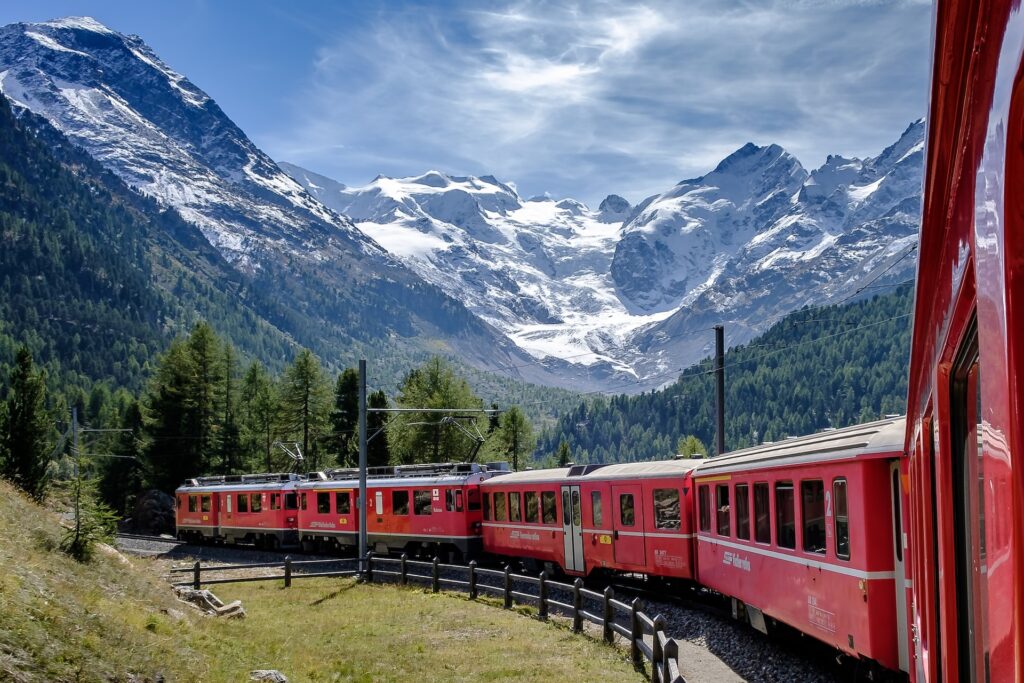 Tren Bernina Express entre verdes paisajes y montañas nevadas al fondo. 