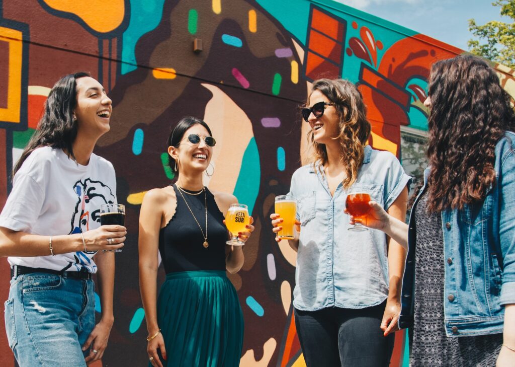 4 mujeres riendo con un vaso de cerveza. Estas experiencias las puedes vivir cuando estés de viaje usando Localeur, una de las apps para tu próximo viaje que recomendamos aquí